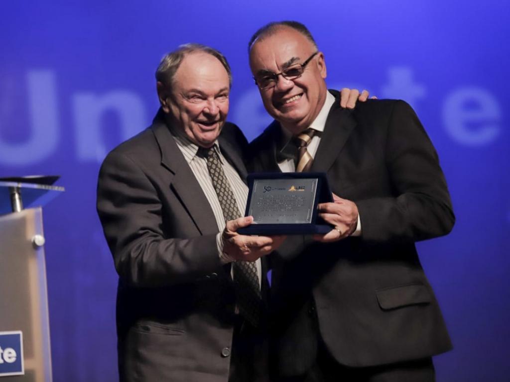 Rietor Genésio Zeferino entrega placa de homenagem ao presidente da UBEC, Pe. José Romualdo Degasperi.