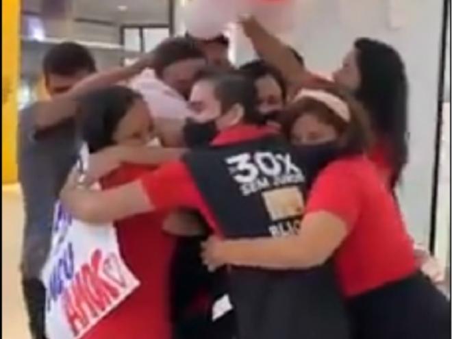 Momento em que o gerente chega para trabalhar e é abraçado pelos funcionários da loja que gerencia 